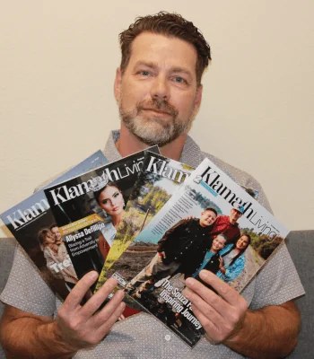Troy Miller, publisher of Klamath Living and founder of Lucky Duck Productions, holding recent issues of the magazine